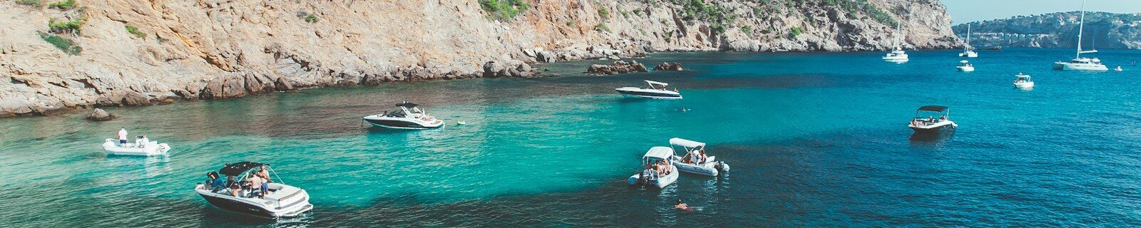 white and blue boat on sea near green mountain during daytime
